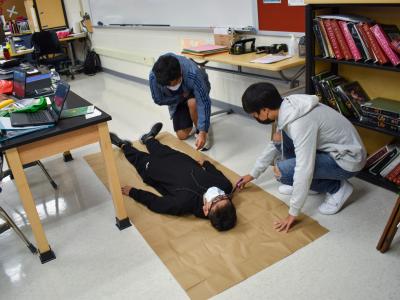 Students trace a classmate's body to create a cutout for measurements.